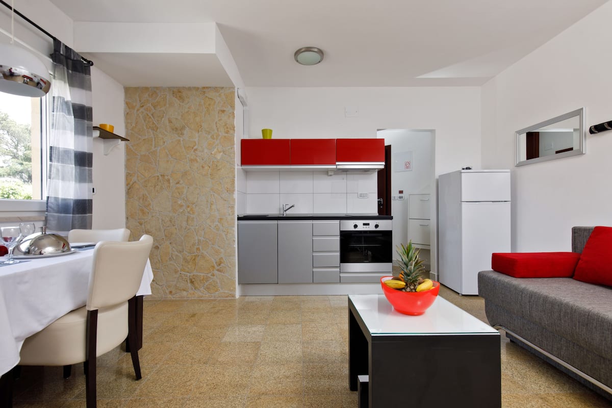 A modern kitchen with red cabinets, a white refrigerator, and a dining area with a table and chairs.