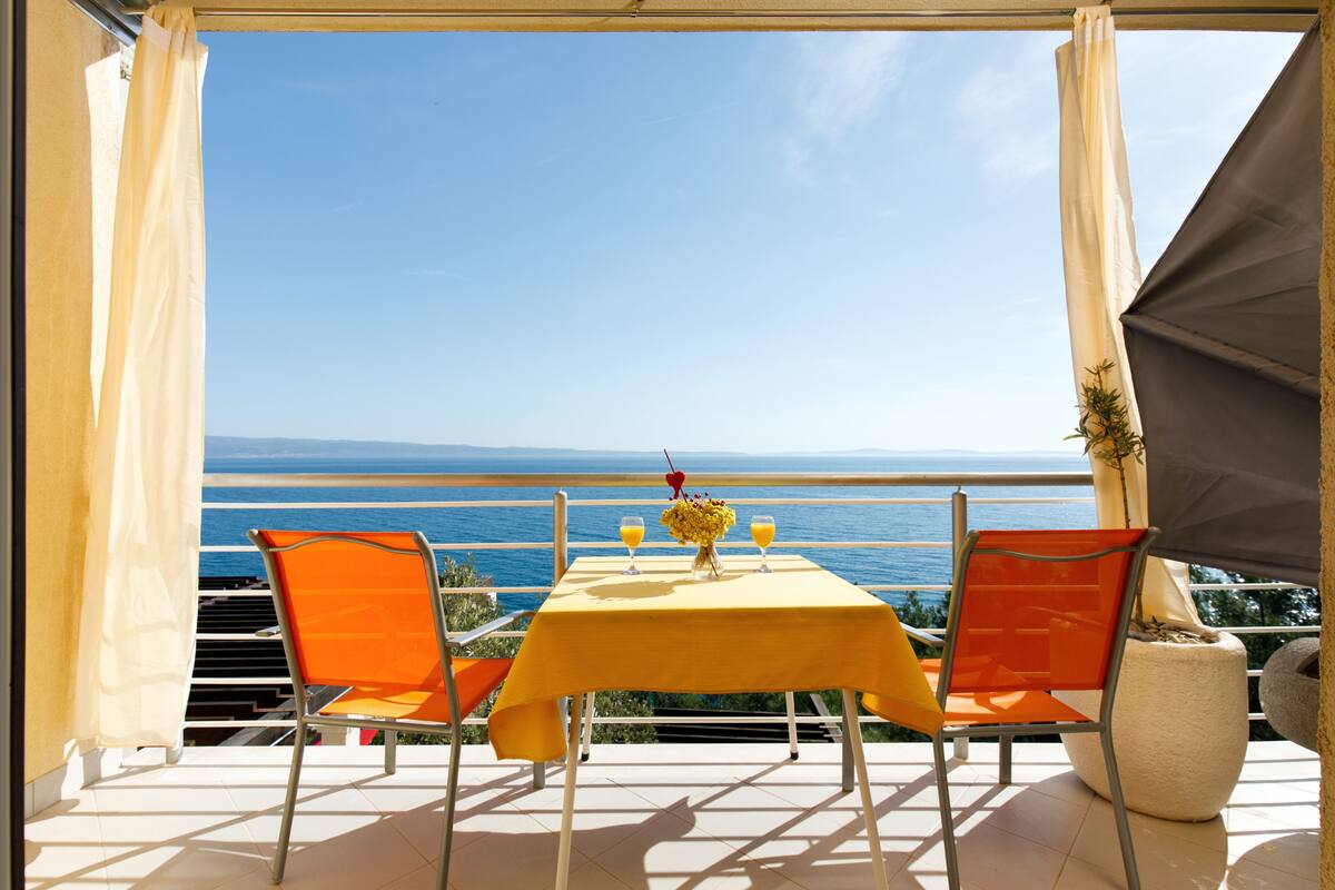 A terrace with a table and chairs, overlooking a body of water.