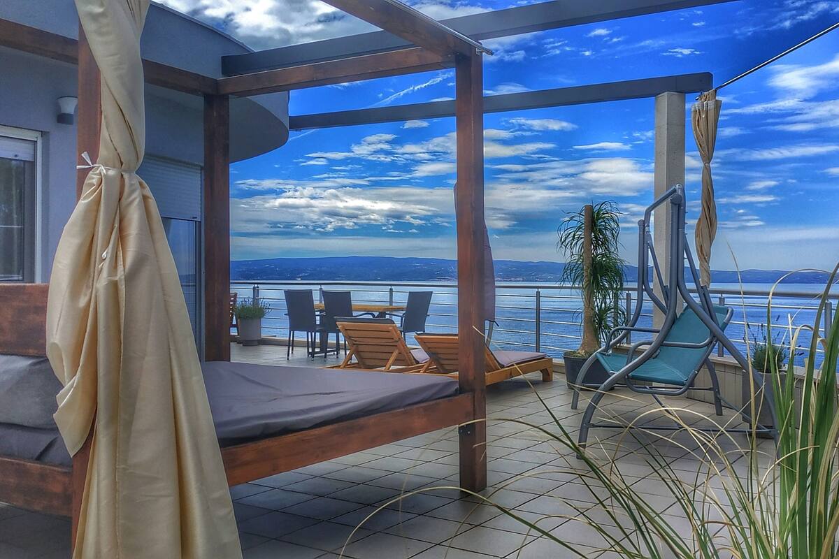 A balcony with a bed, lounge chairs, and a view of the sea.