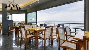 A restaurant with wooden tables and chairs, large windows with a view of the sea, and a modern chandelier. - Ark Beach Hotel (Split)