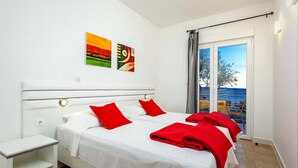 A hotel room with a bed, two red pillows, a white headboard, and two paintings on the wall. - Ark Beach Hotel (Split)