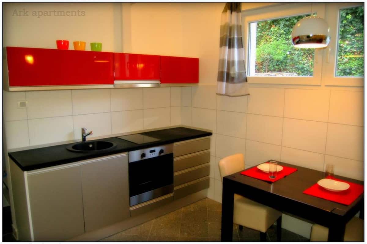 A compact kitchen with a black countertop, stainless steel appliances, and a dining area with a table and chairs.