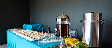 A buffet table with a coffee station, a box of napkins, and a potted plant.