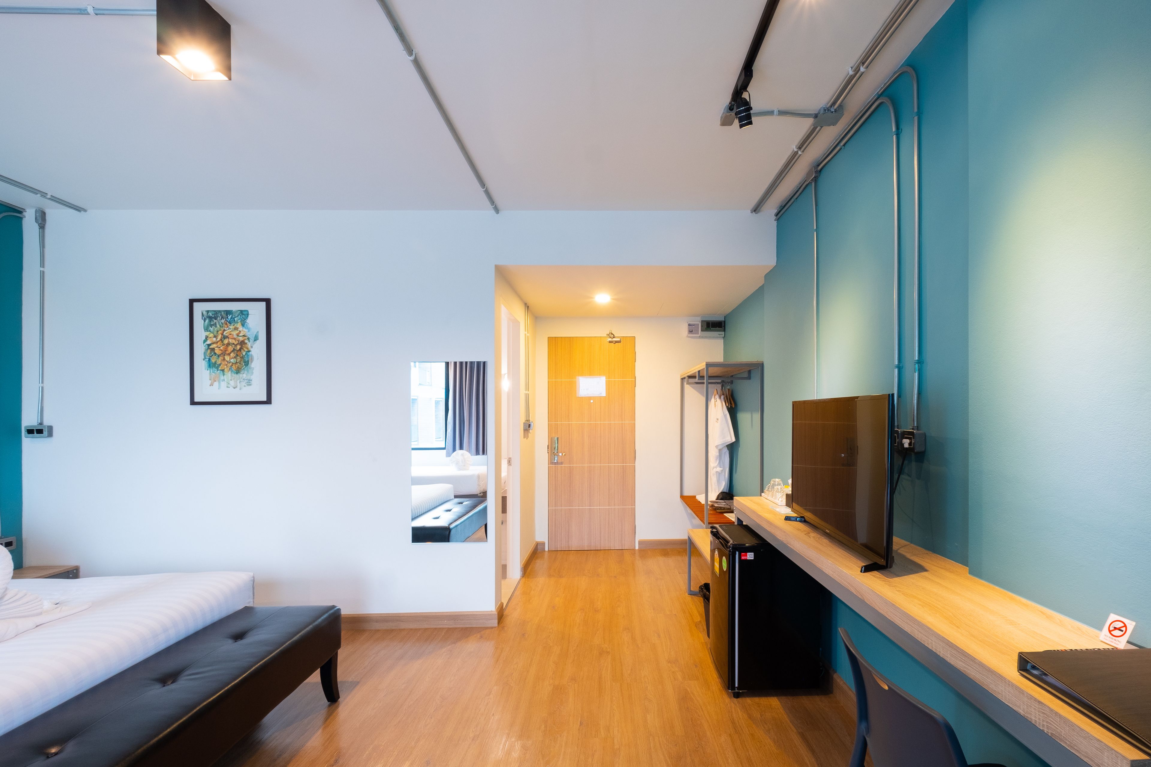 A modern hotel room with a bed, a desk with a computer, a TV, and a bathroom visible through an open door.