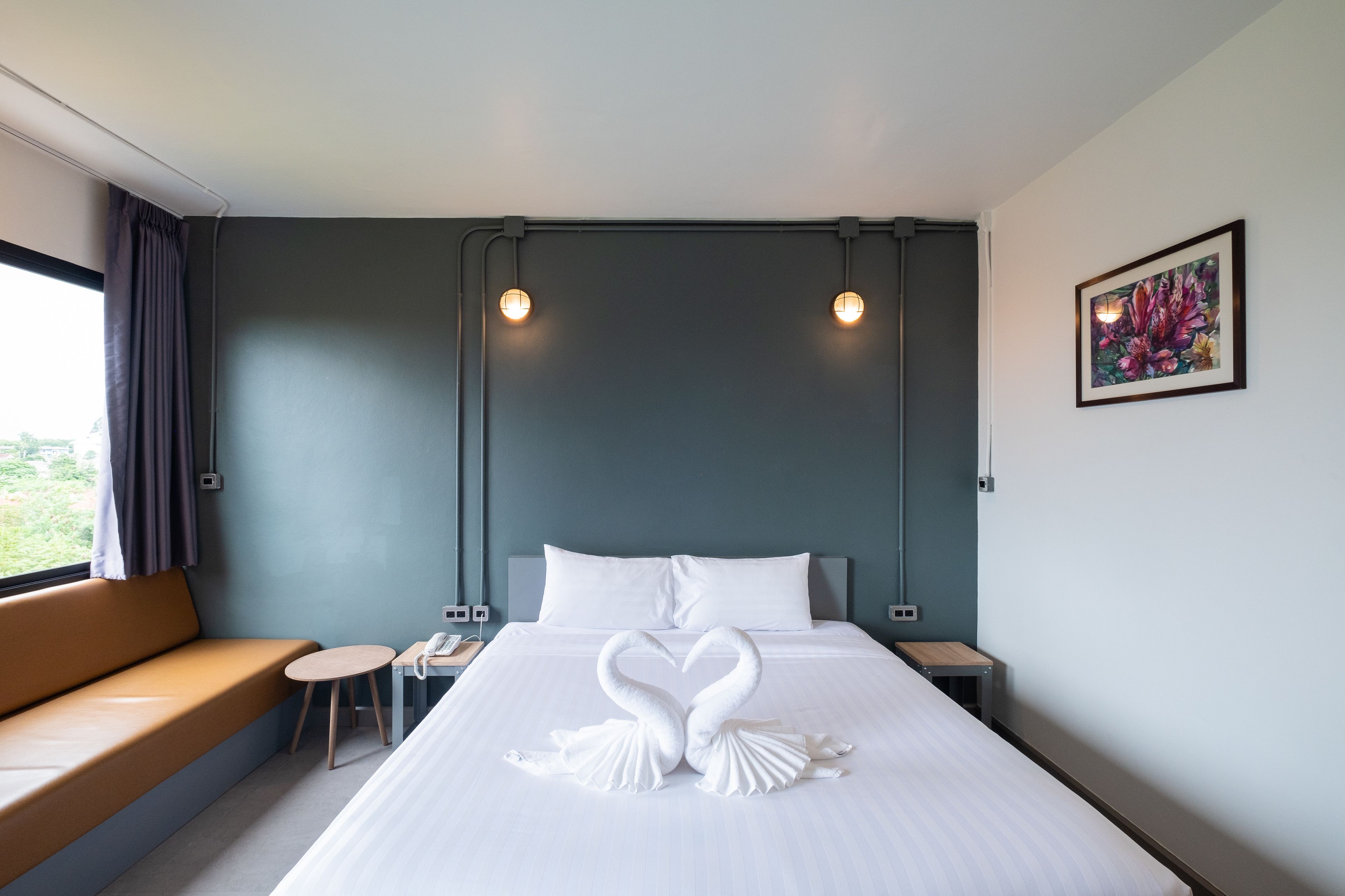 A hotel room with a bed, a bench, a small table, and a painting on the wall.