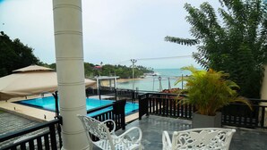 A pool area with two white chairs, a beige umbrella, and a view of the beach. - Queens Beach Hotel (Tangalle)
