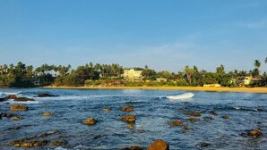 A coastal view with rocky waters, palm trees, and buildings along the shore. - Queens Beach Hotel (Tangalle)