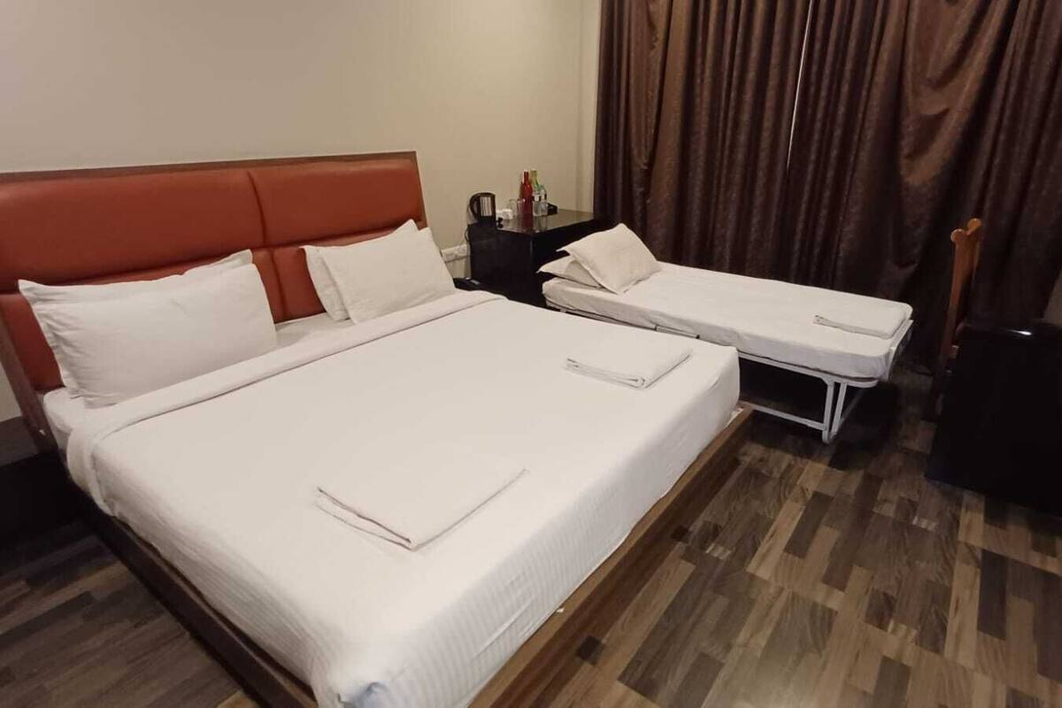 Une chambre d’hôtel avec un grand lit, deux petits lits, un plancher en bois, un bureau avec un ordinateur et une télévision.