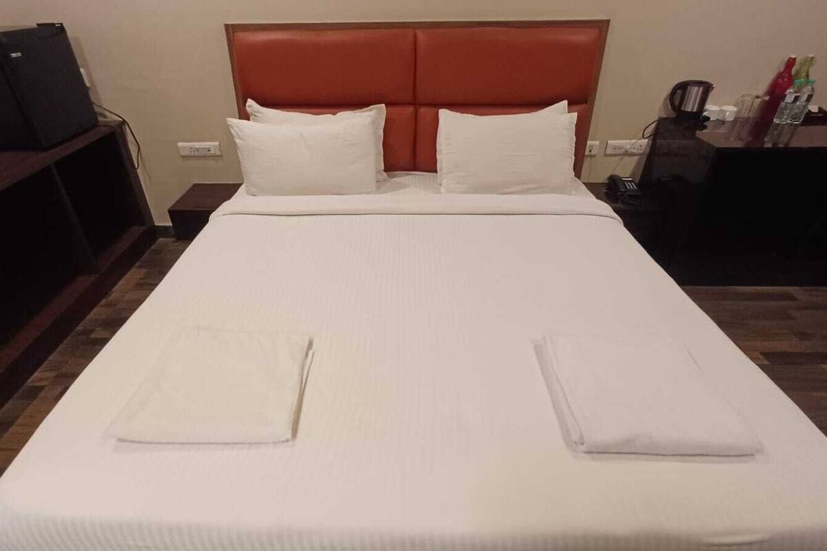 Un lit bien fait, avec des draps blancs, une tête de lit en bois et deux oreillers.