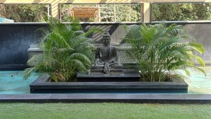 A Buddha statue in a garden setting with a pool and palm trees. - Hotel Sriram JB Residency (Virudhunagar)