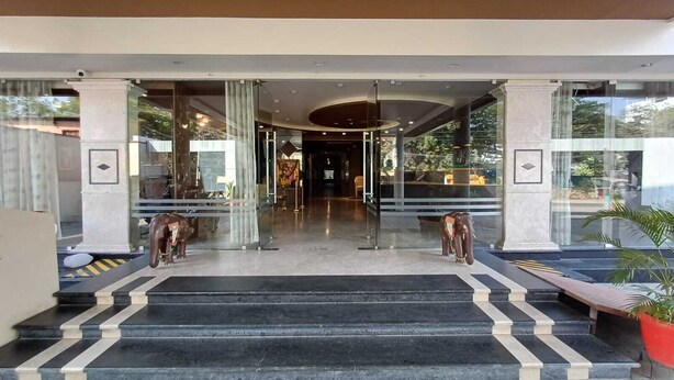 A hotel entrance with a glass facade, a marble staircase, and two elephant statues. - Hotel Sriram JB Residency (Virudhunagar)