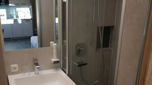 A modern bathroom with a glass-enclosed shower, a sink with a mirror, and a cabinet below. - Ferienhaus Mott (Lermoos)