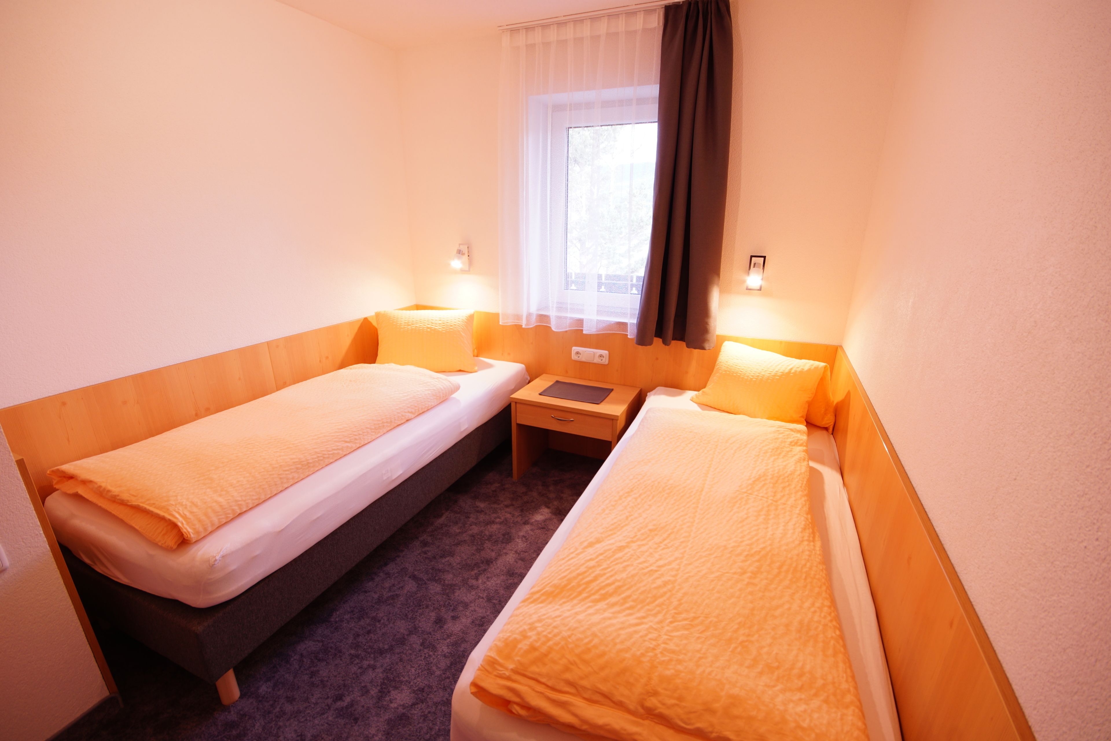 A small hotel room with two single beds, a nightstand, and a window with curtains.