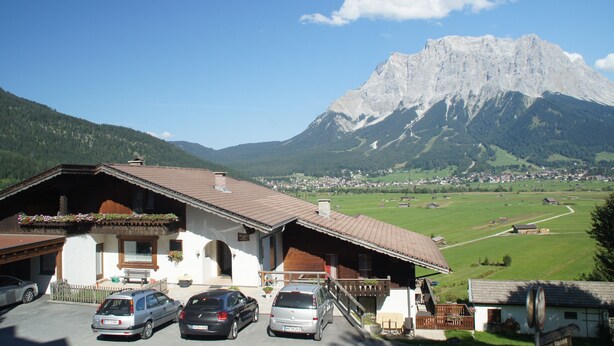 A mountain chalet with a parking area, a small garden, and a view of a mountain range. - Ferienhaus Mott (Lermoos)