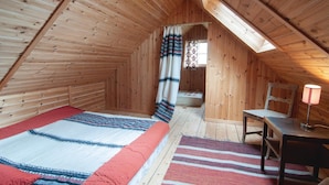 Et hyggeligt soveværelse på loftet med trævægge, skråvæg, seng med mønstrede tæpper, en stol, et bord og en lampe.