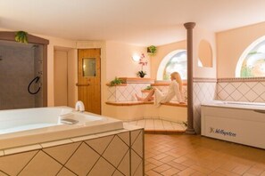 A bathroom with a bathtub, a shower, and a toilet. There is a wooden door, a window with a view, and a towel rack. - Hotel-Restaurant Bastenhaus (Dannenfels)