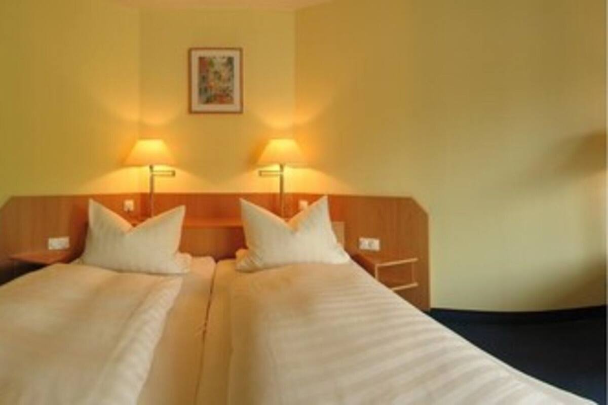 Een hotelkamer met twee eenpersoonsbedden, een stoel, een bureau en twee wandlampen.