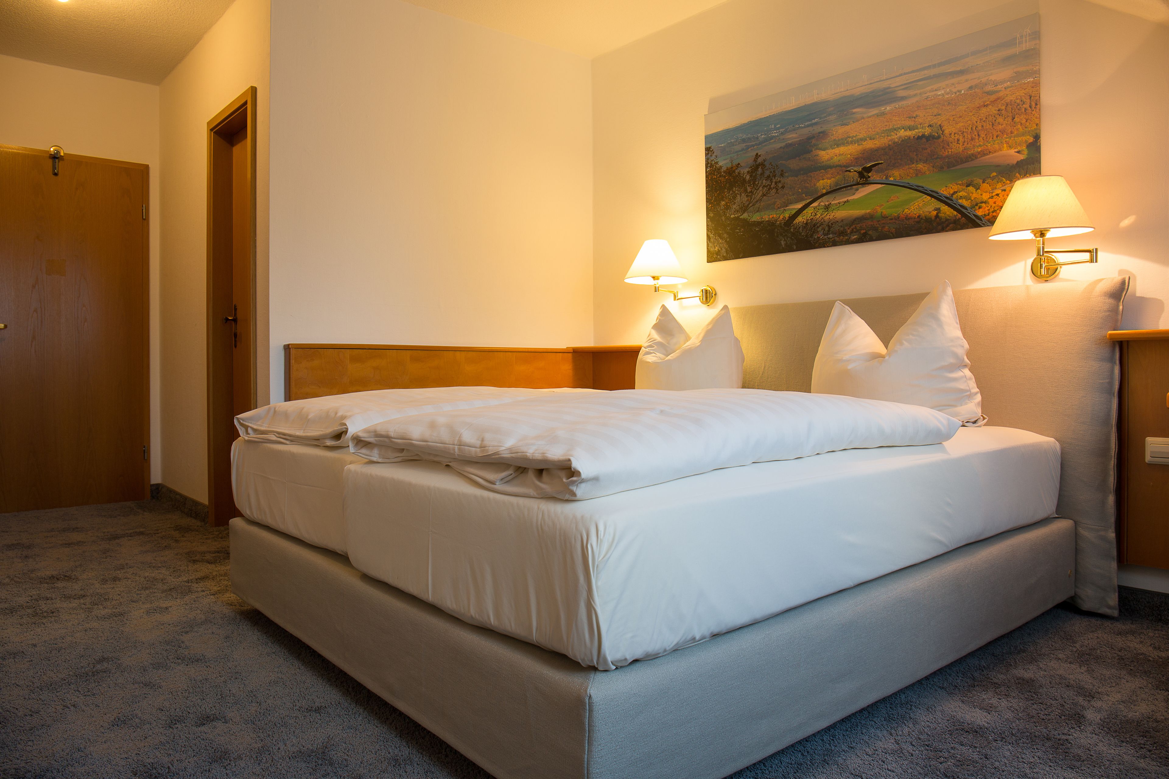A neatly made bed with white linens, a headboard, and two wall-mounted lamps on either side.