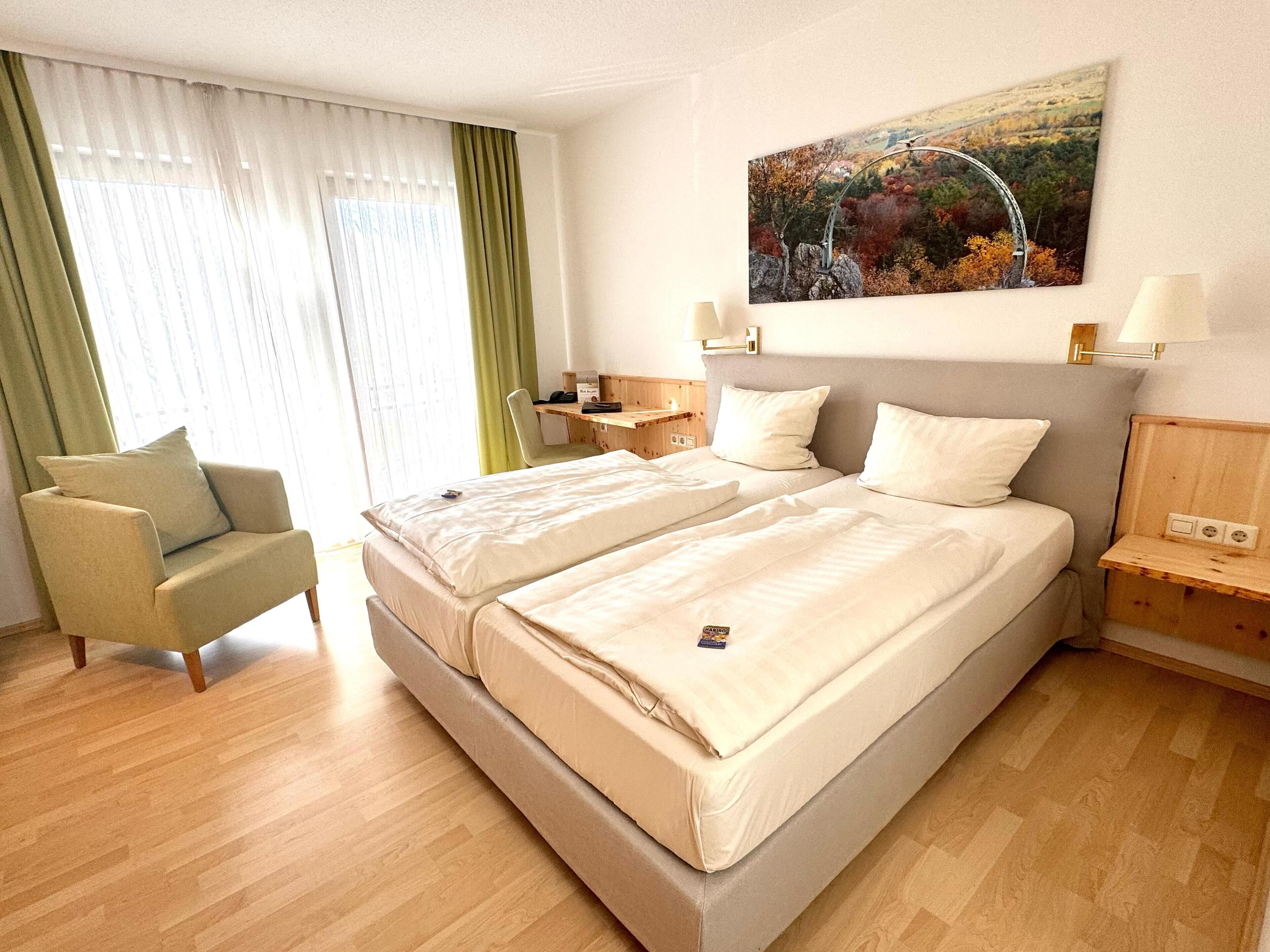 Ein Hotelzimmer mit Doppelbett, einem Sessel, einem Schreibtisch und einem Bild an der Wand.