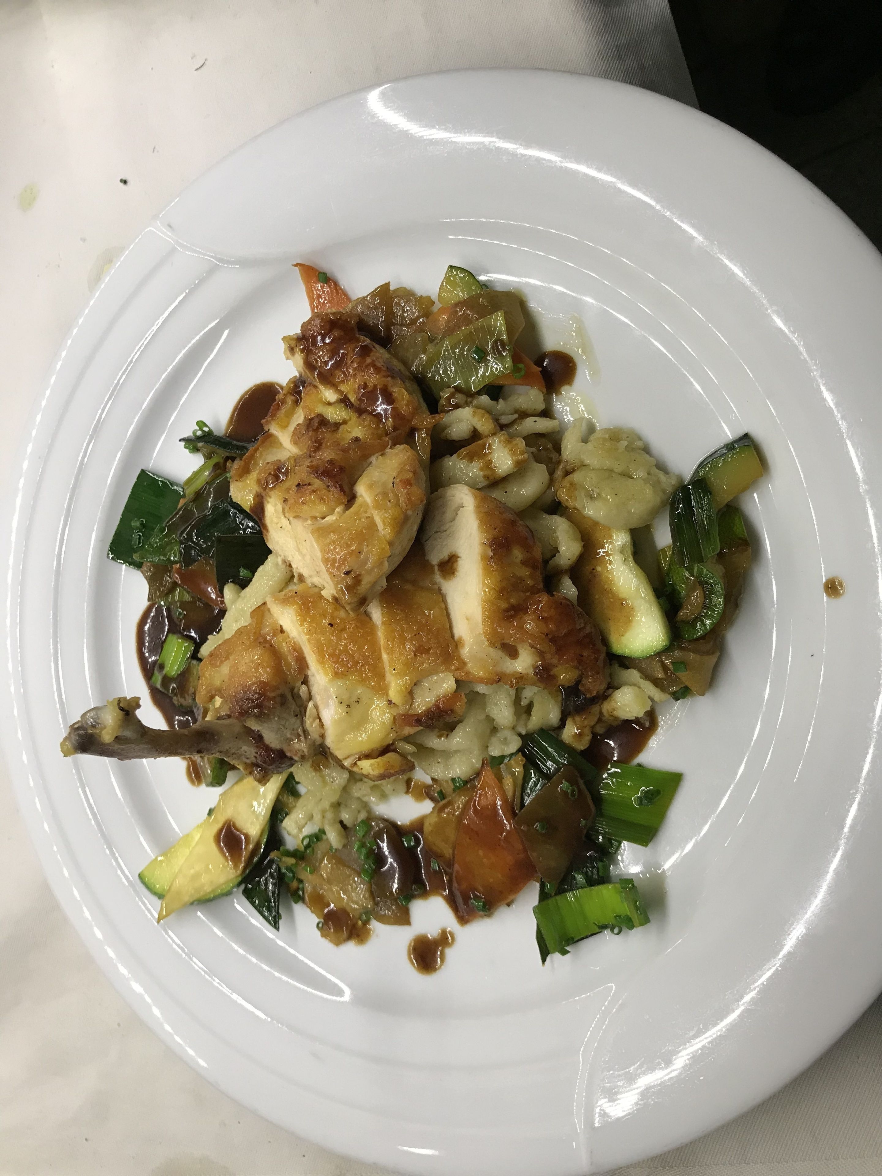 Ein weißer Teller mit gegrilltem Hähnchen, Gemüse und Soße.