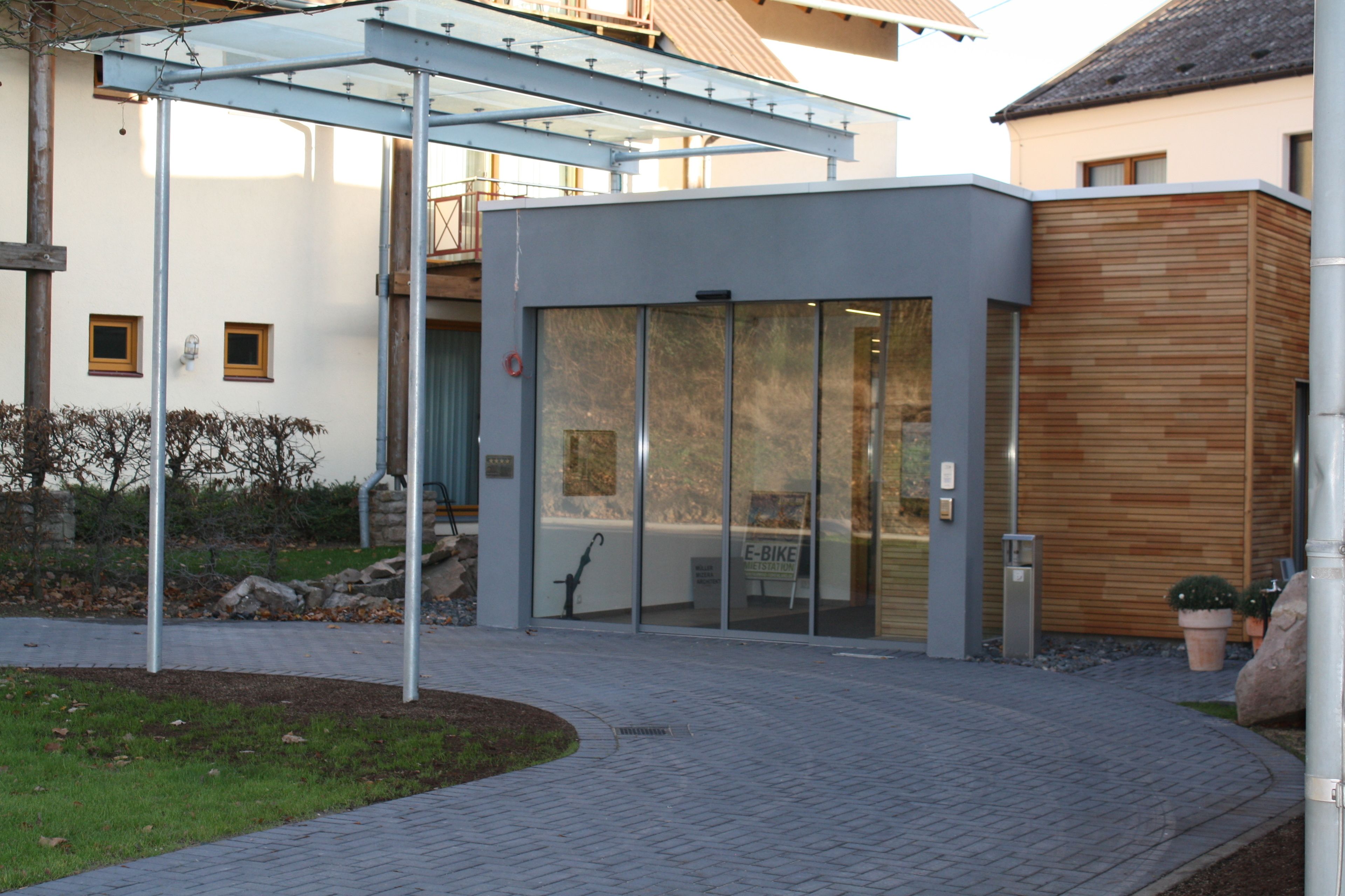 A modern building with a glass entrance, a wooden facade, and a metal structure overhead.