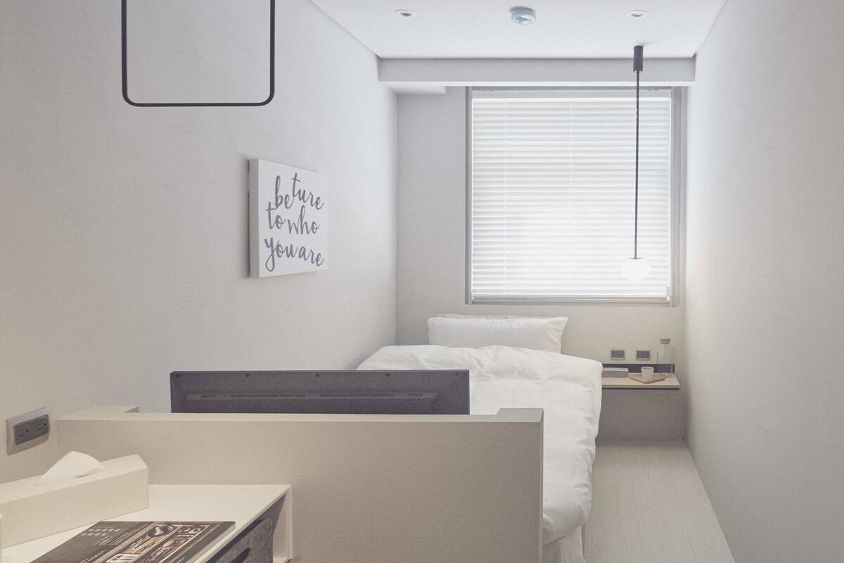 A modern bedroom with a single bed, a bedside table, a nightstand, and a window with blinds.