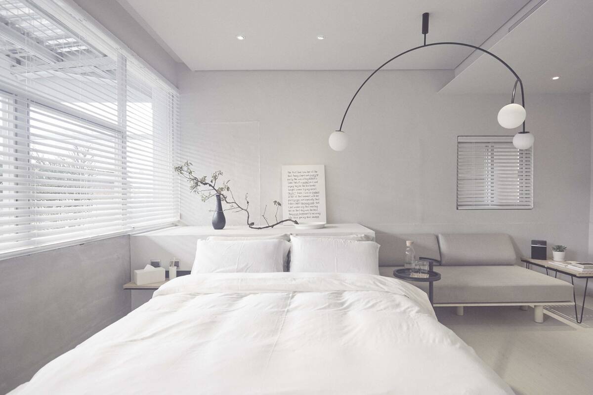 A modern bedroom with a large bed, bedside tables, a reading chair, and a wall-mounted lamp.
