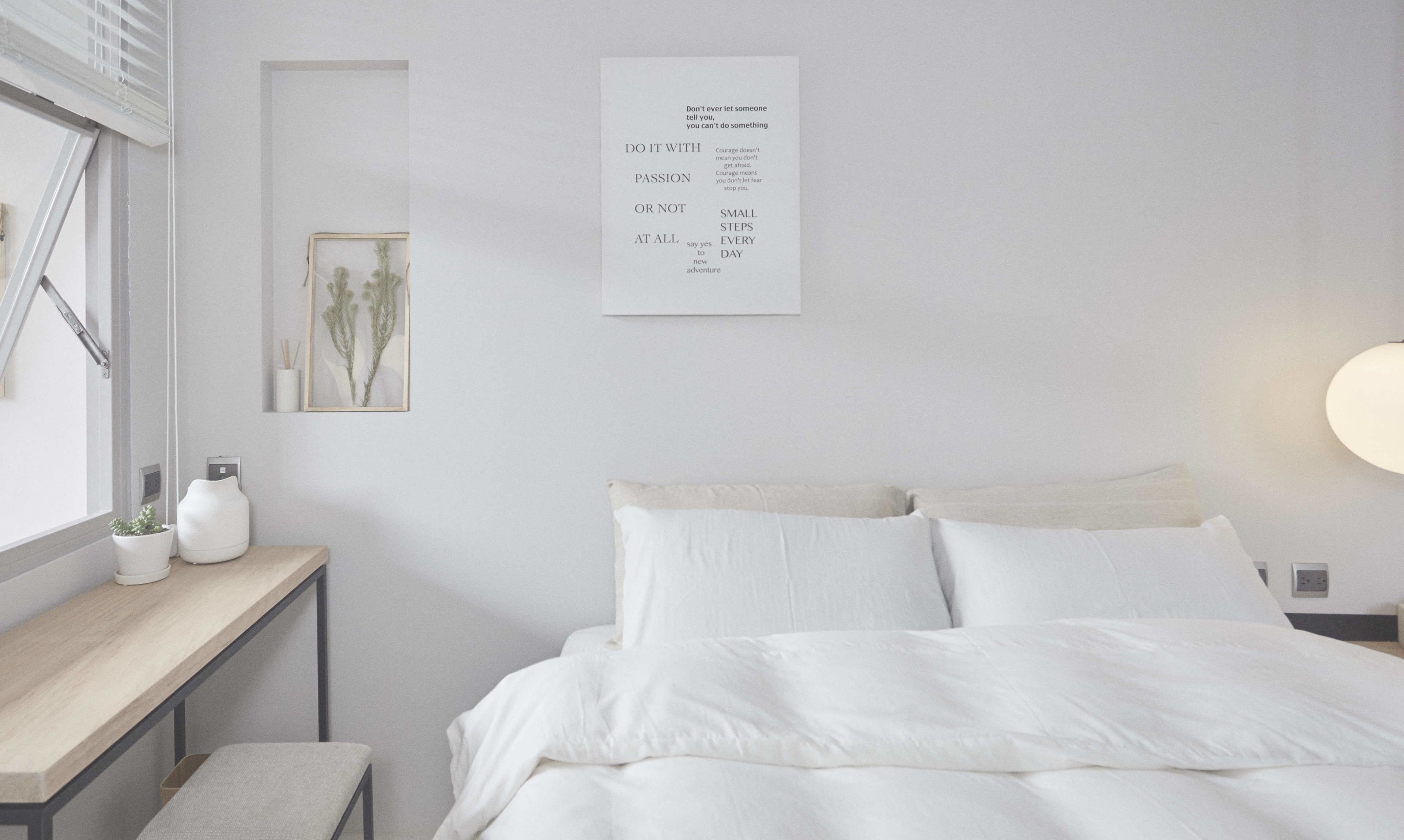 A minimalist bedroom with a bed, bedside table, and a wall-mounted motivational poster.