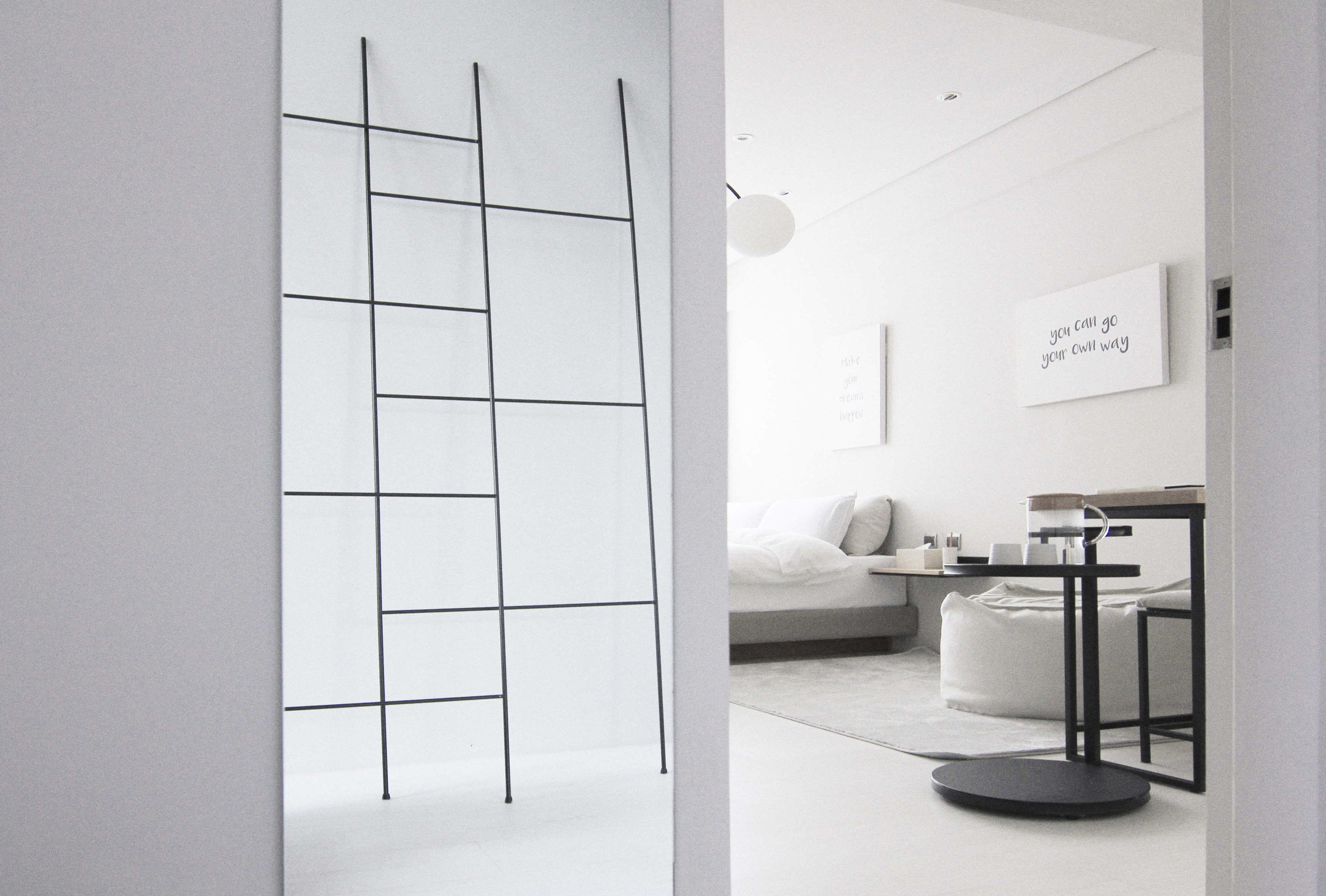 A modern, minimalist room with a white sofa, a small round table, and a ladder-like structure against the wall.