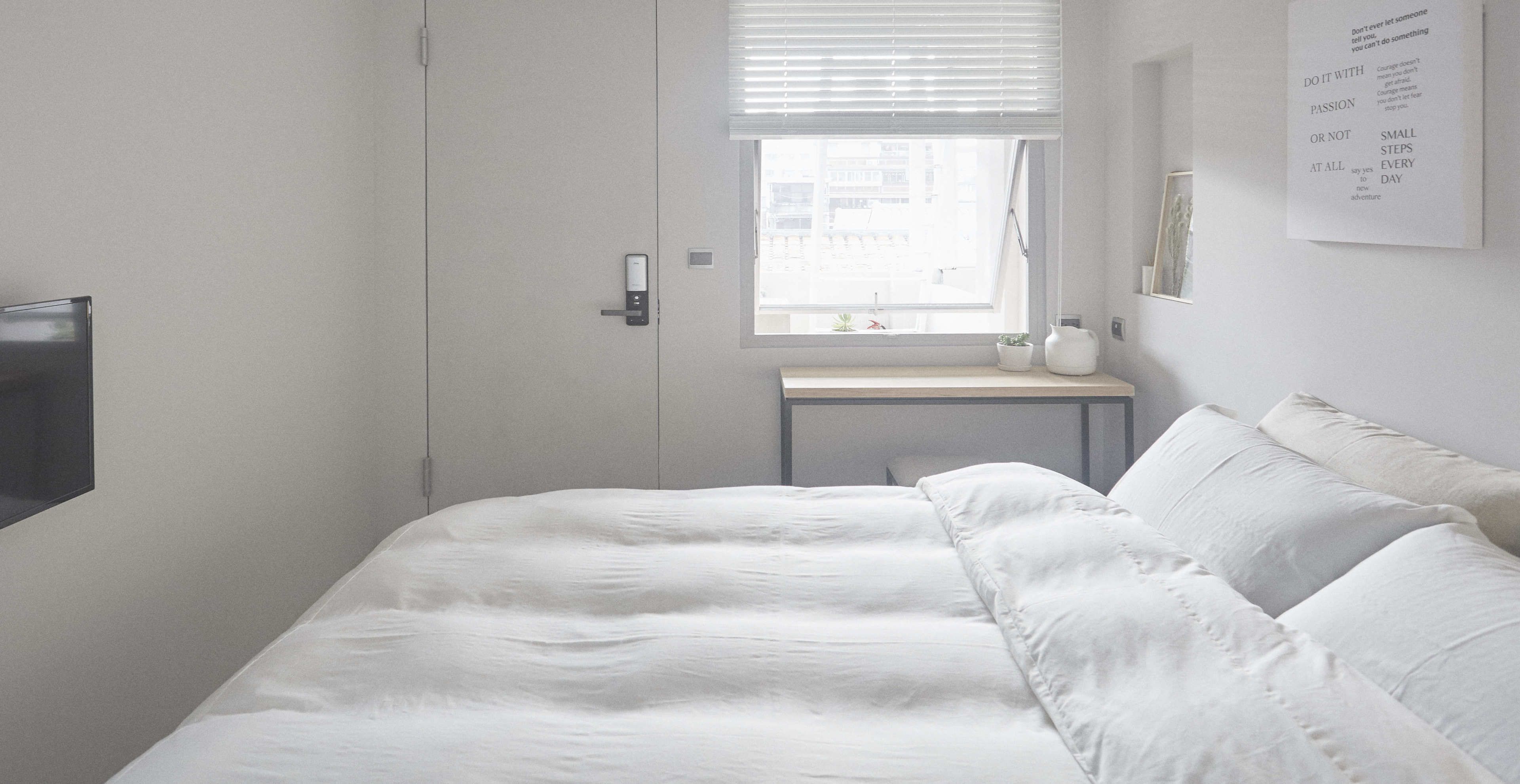 A minimalist bedroom with a bed, a bedside table, and a window with blinds.