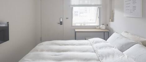 A minimalist bedroom with a bed, a bedside table, and a window with blinds.