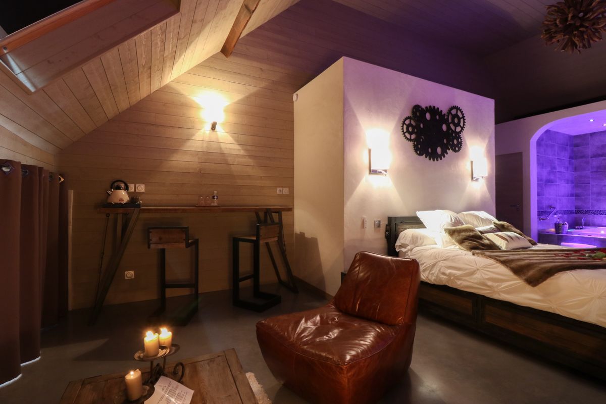 A cozy bedroom with a wooden ceiling, a bed with white linens, a leather chair, and a small table with candles.