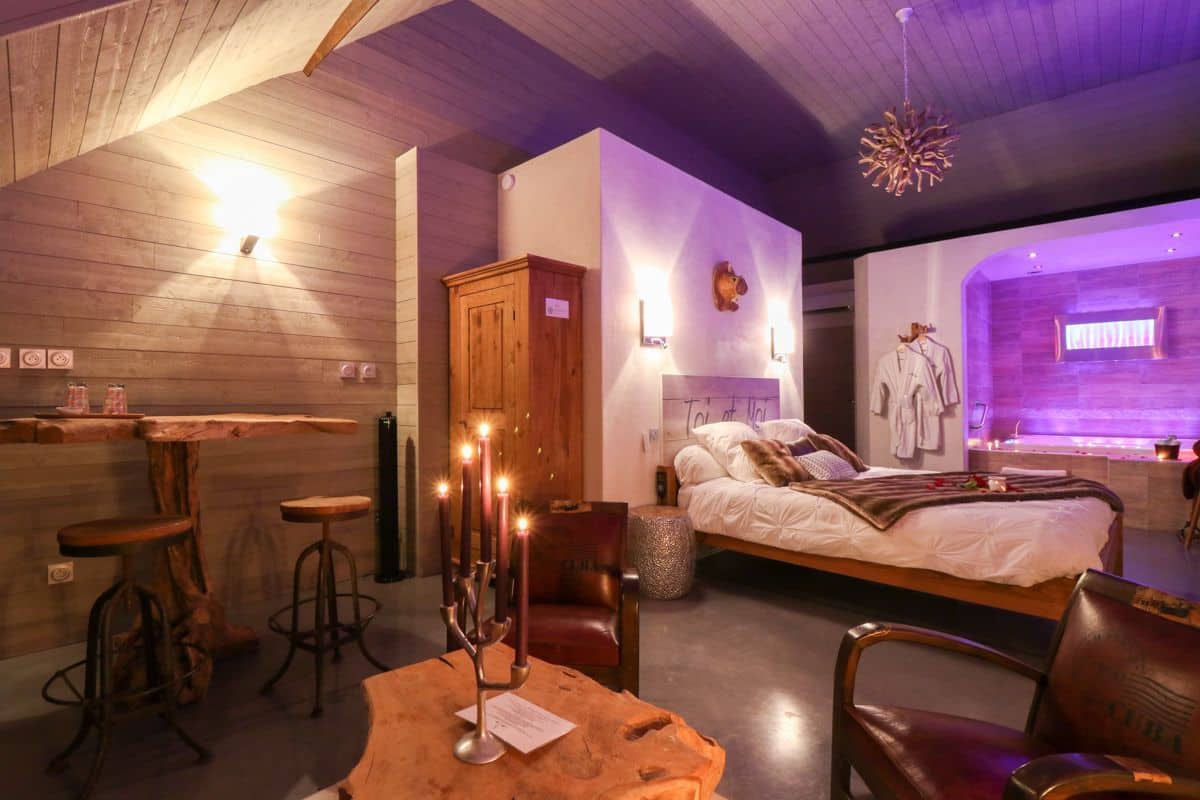 A cozy room with a wooden ceiling, a bed with white linens, a wooden cabinet, and a bar area with stools.