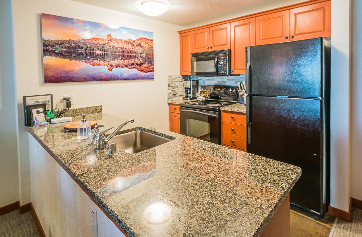 Una cocina con encimeras de granito, refrigerador de acero inoxidable y armarios color naranja.
