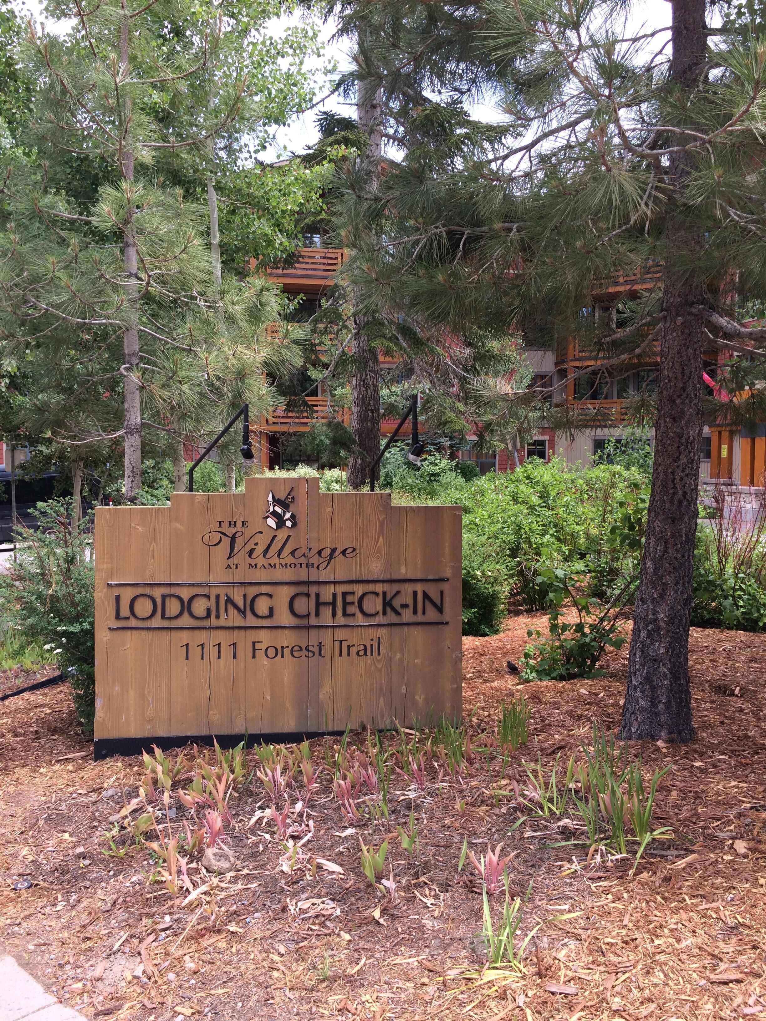 A wooden sign for The Village at Mammoth Lodge Check-In, indicating the location as 1111 Forest Trail.