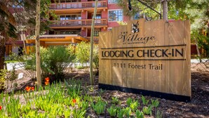 A wooden sign with "Lodging Check-In" and "The Village at Mammoth" text, indicating a lodging area. - Modern Condo in Heart of Village, 1st floor, Steps to Gondola & all Amenities   (Mammoth Lakes)