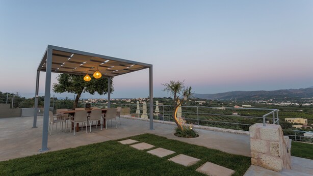 Un patio al aire libre con pérgola, mesa de comedor, sillas y vista del paisaje.