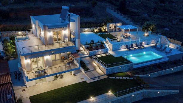 Une maison moderne à deux étages, dotée d’une piscine, d’un espace extérieur aménagé et d’un patio bien éclairé.