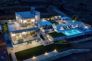 Une maison moderne à deux étages, dotée d’une piscine, d’un espace extérieur aménagé et d’un patio bien éclairé.