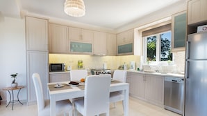 Une cuisine moderne avec des meubles blancs, un réfrigérateur en acier inoxydable et un coin repas comprenant une table et des chaises blanches.