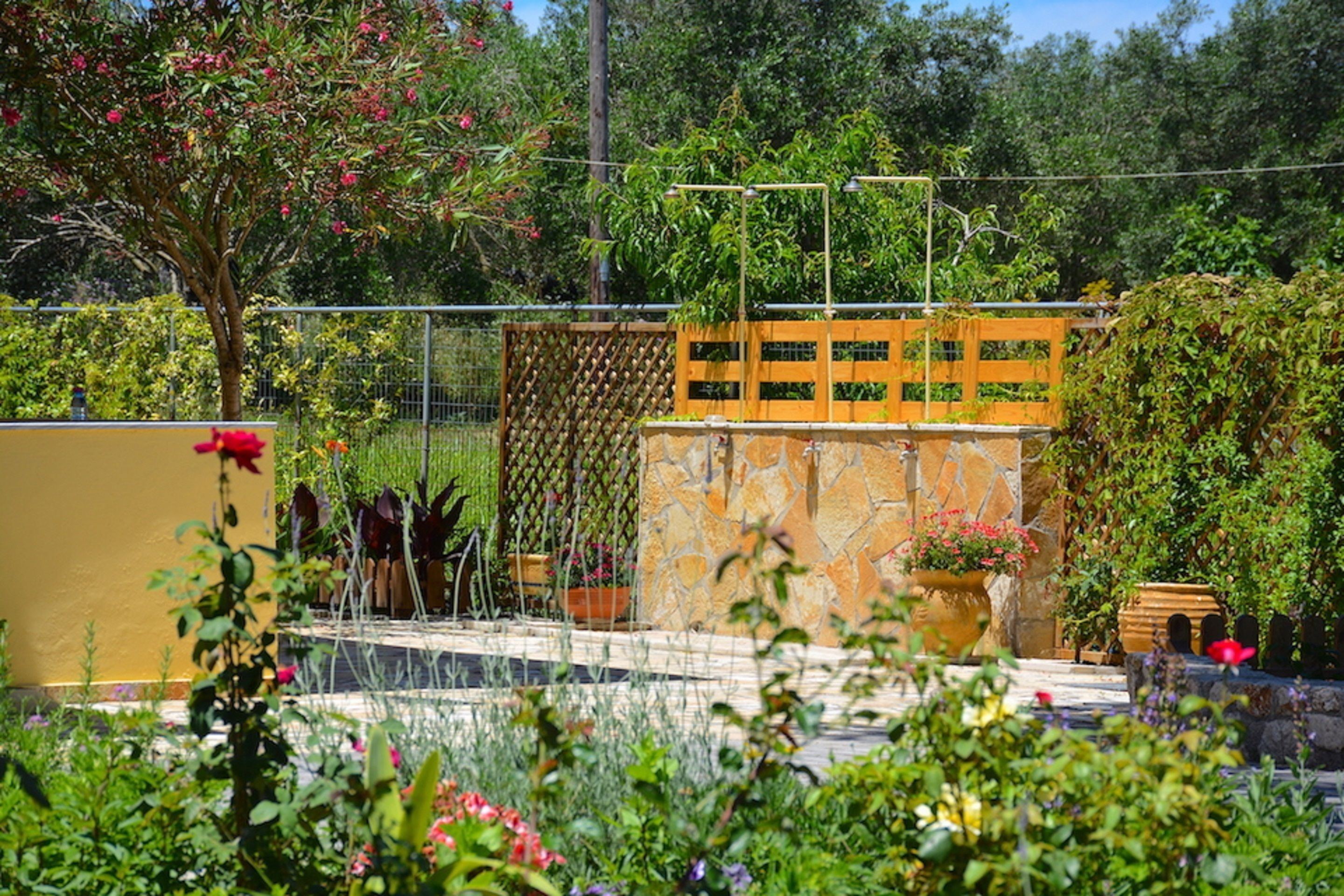Um jardim com diversas plantas e flores, uma cerca de madeira e um muro de pedra.