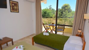 A room with two beds, a small table, and a view of greenery outside. - Alexandra Apartments (Corfu)