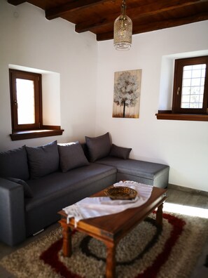 A living room with a grey sofa, a wooden coffee table, and a painting of a tree. - Effrosini Stonehouse Portaria (Volos)