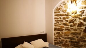 Camera da letto con parete in pietra, testiera in legno e letto con copriletto blu e cuscini bianchi.