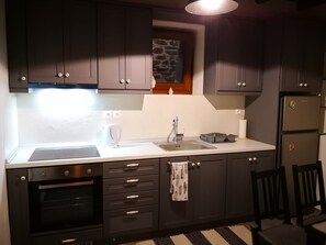 A modern kitchen with dark cabinets, a built-in oven, a sink, and a refrigerator. - Effrosini Stonehouse Portaria (Volos)