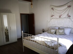 A bedroom with a white bed, a nightstand, a wardrobe, and a hanging light fixture. - Effrosini Stonehouse Portaria (Volos)