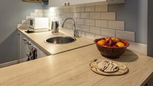 Una cocina con un lavamanos, un microondas y un tazón de fruta en la encimera.