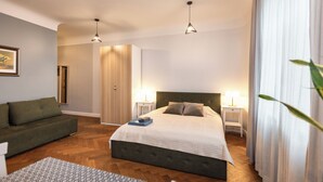 Un dormitorio con cama, mesitas de noche, un sofá, una mesa de comedor y vistas al exterior.