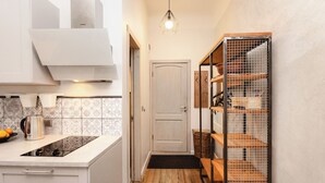 Una cocina estrecha con piso de madera, armarios blancos y una estantería de metal.