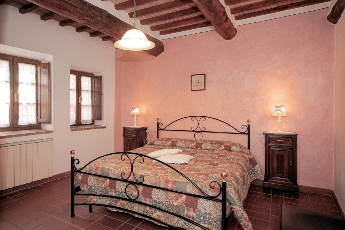 Ein Schlafzimmer mit einem Metallbettgestell, zwei Nachttischen mit Lampen, einem Heizkörper und Holzbalken an der Decke.